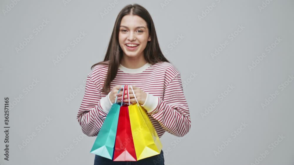 Smiling attractive brunette woman holding packages and rejoicing over grey background Smiling attractive brunette woman holding packages and rejoicing over grey background
