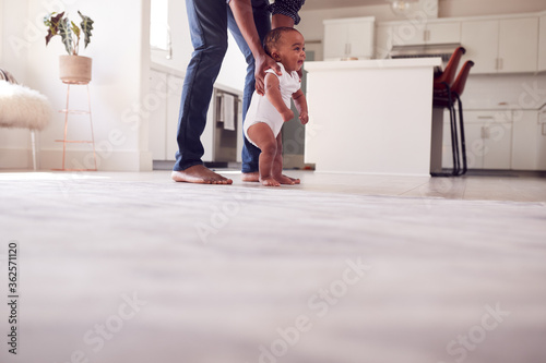 Father Encouraging Smiling Baby Daughter To Take First Steps And Walk At Home