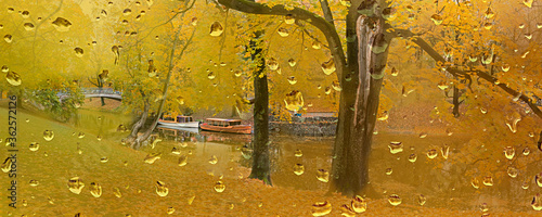 Autumnal landscape with park, pleasure boats at river, all seen through window with drops of rain 