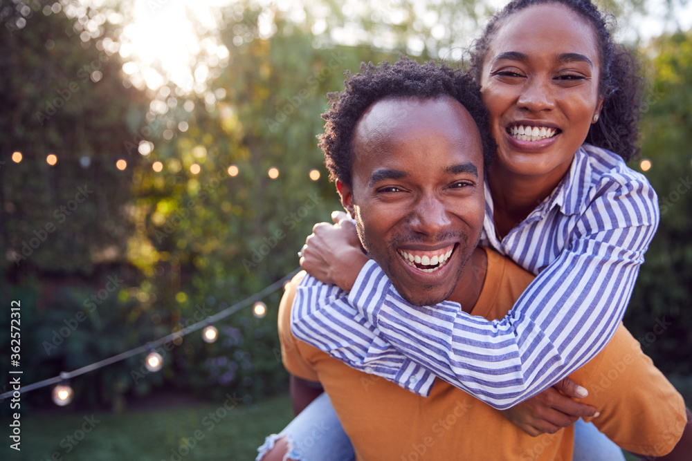 Portrait Of Couple With Man Giving Woman Piggyback At Home In Back garden Portrait Of Couple With Man Giving Woman Piggyback At Home In Back garden