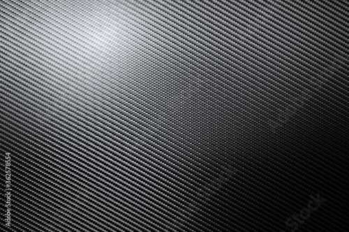 Structural detail of an industrial carbon fibre sheet in a full frame view showing the repeat diagonal pattern as light plays across the surface in a background texture