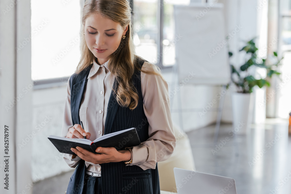 beautiful businesswoman writing in notebook while standing in office beautiful businesswoman writing in notebook while standing in office