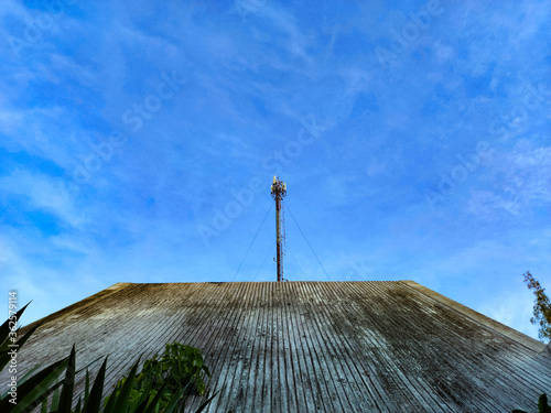 The pole stands tall on the roof of the house. With a blue sky as a background