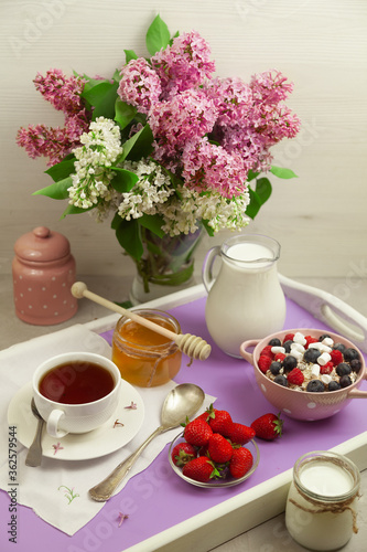 Breakfast with strawberries  blueberries and raspberries with flakes  honey  milk and tea  decorated with lilac.