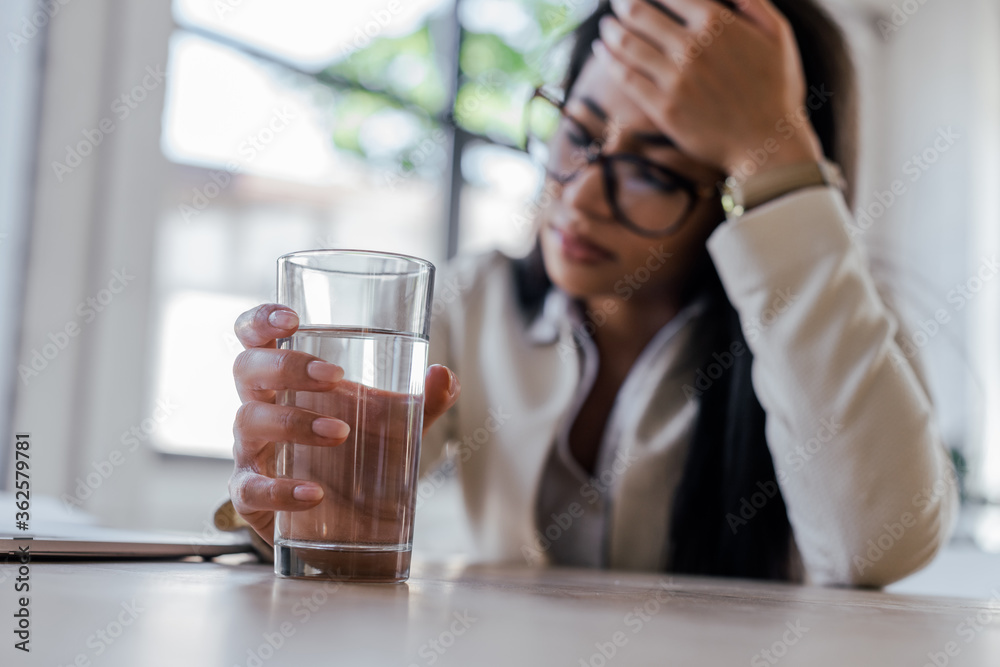 selective focus of tired businesswoman holding glass of water in office selective focus of tired businesswoman holding glass of water in office