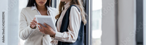 panoramic concept of businesswoman holding digital tablet near coworker