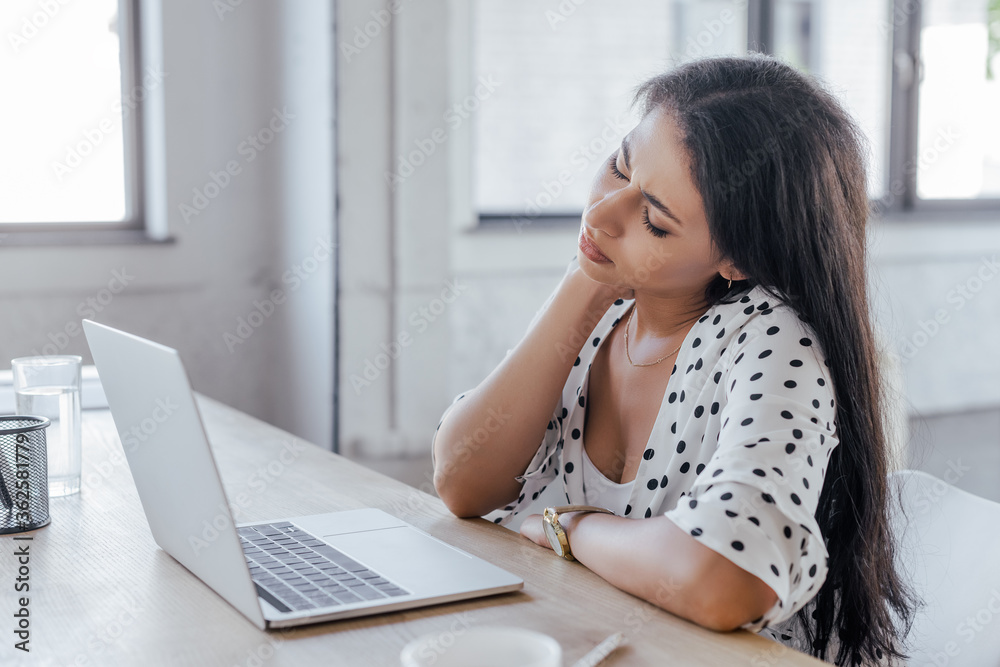 selective focus of beautiful businesswoman touching neck while suffering from pain in office