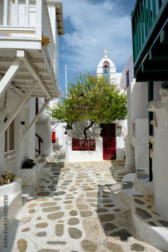 Fototapeta Naklejka Na Ścianę i Meble -  Picturesque scenic narrow Greek streets with traditional whitewashed houses with blue doors windows of Mykonos town and orthodox church in famous tourist attraction Mykonos island, Greece