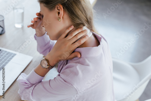 selective focus of businesswoman touching neck while feeling pain in office