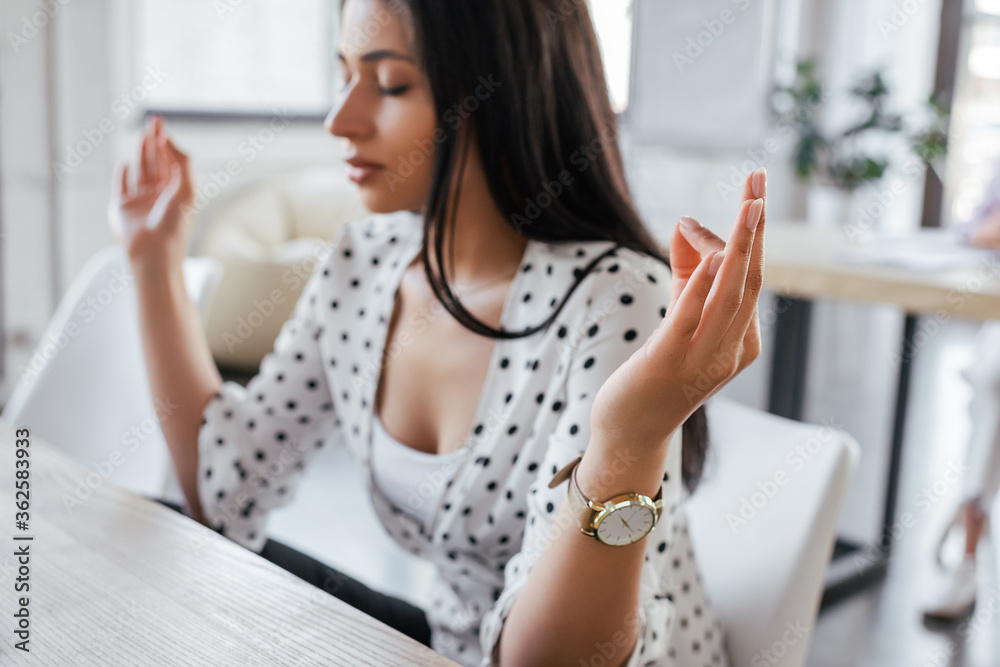 selective focus of beautiful businesswoman with closed eyes meditating in office