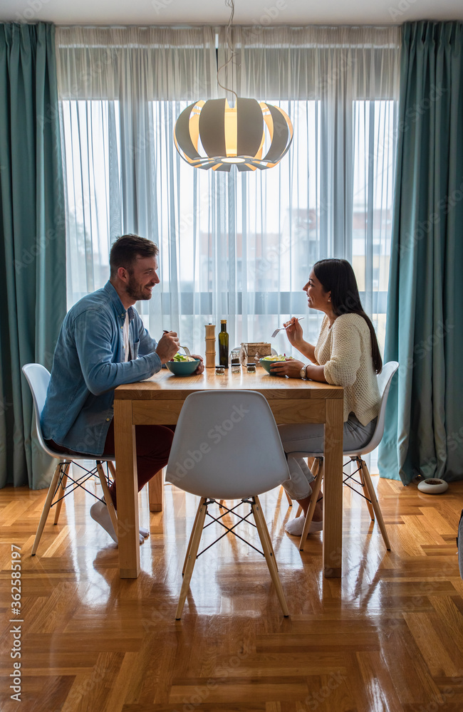 Young couple eating salad while sitting at a table at home. Young couple eating salad while sitting at a table at home.