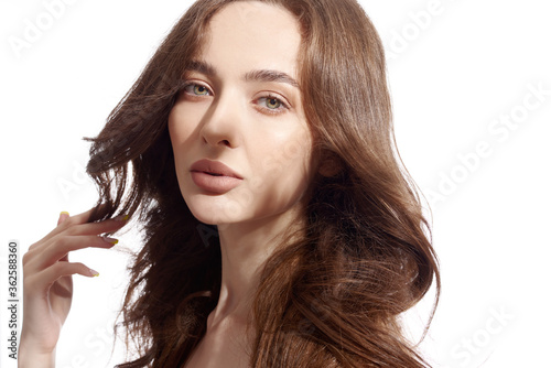 Beautiful young brunette with natural make-up and silk long hair on a white background. Shadow on the face. Woman looking at camera. Isolated over white background.