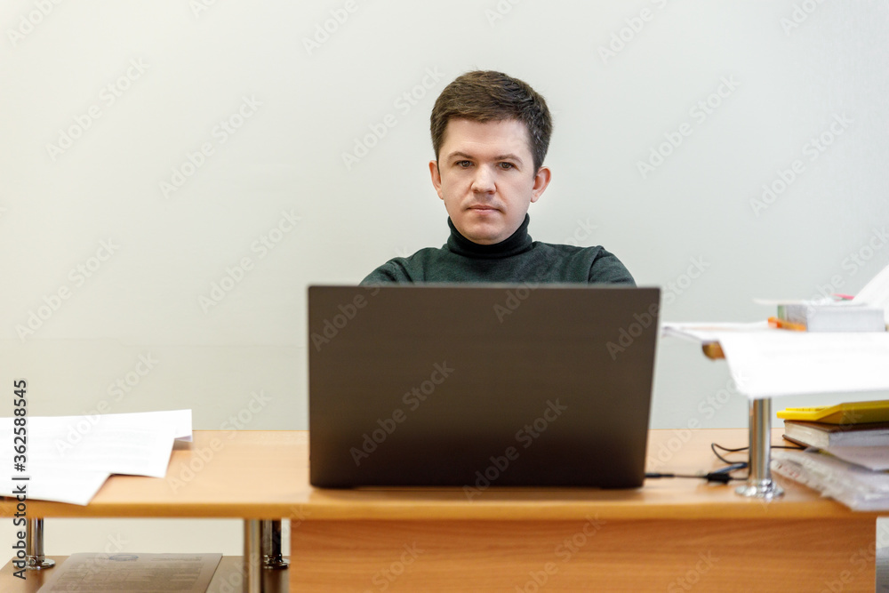 A casual businessman works in an office, sits at a Desk, types on a keyboard, looks at a computer screen. Concept of office work. A casual businessman works in an office, sits at a Desk, types on a keyboard, looks at a computer screen. Concept of office work.