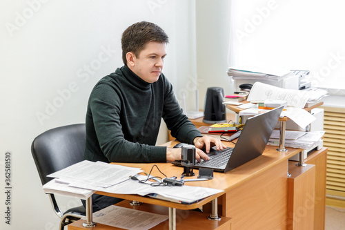 A casual businessman works in an office, sits at a Desk, types on a keyboard, looks at a computer screen. Concept of office work.