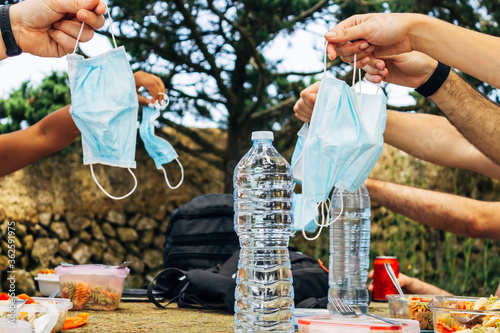 Fototapeta Naklejka Na Ścianę i Meble -  A Several hands holding face masks in picnic with water and soda. Camping picnic in the new normal, Covid 19.