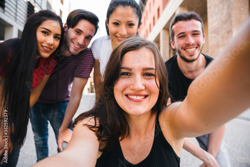 Group of best friends taking a selfie with smartphone in the city - Millennial having fun in summer together - Portrait of people in the street in a moment of break and relax © loreanto