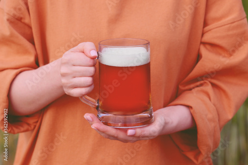Close-up of women's hands with a mug of dark craft beer with foam outdoors.Brewing.Oktoberfest.International beer day.The concept of bad habits