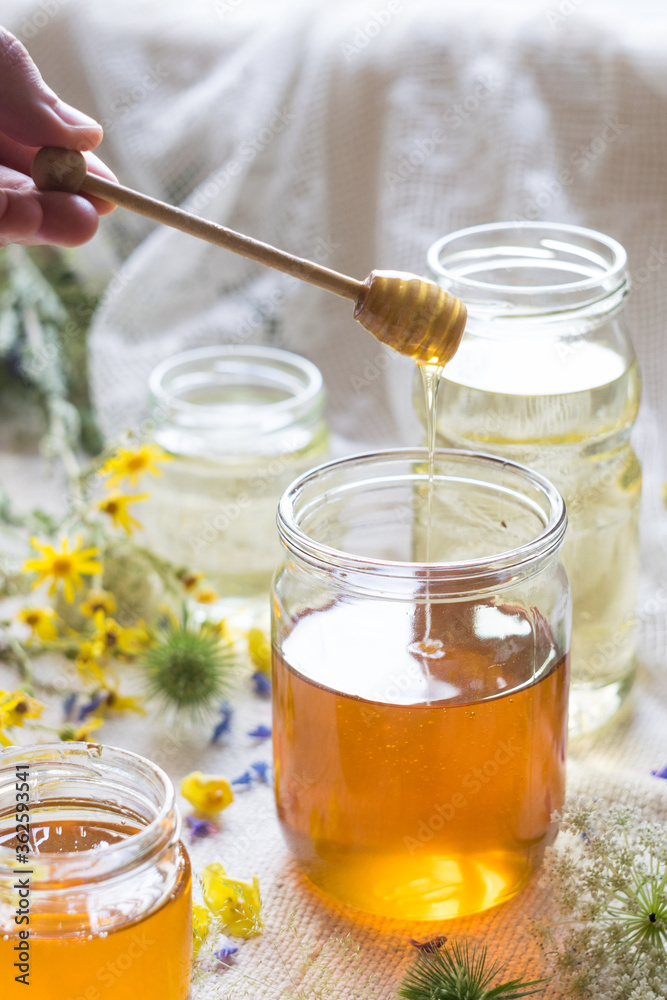 A honey jar with a spoon for honey in hand with flowers in background, selektive focus, backlight A honey jar with a spoon for honey in hand with flowers in background, selektive focus, backlight