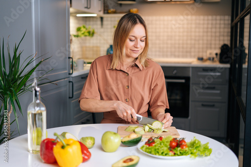 Young smiling vegetarian woman preparing healthy vegan food alone at home. Attractive fit girl prepare healthy dinner  make surprise for husband. Healthy food lifestyle concept.