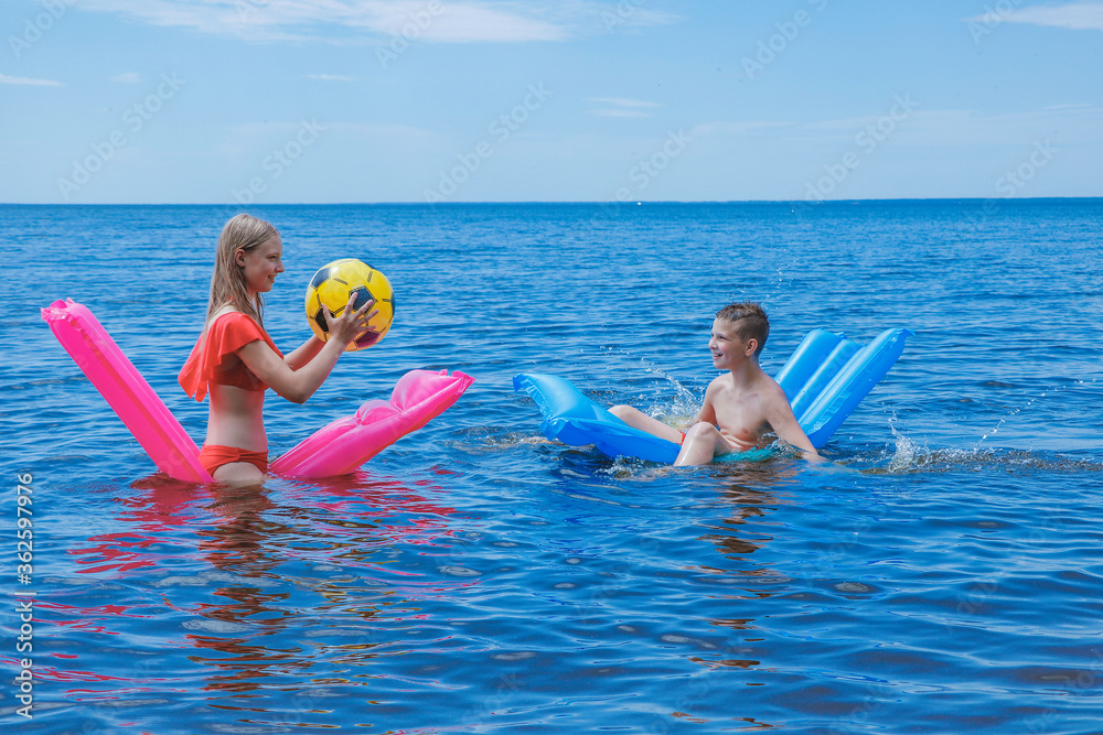 children on the beach relax and have fun in the summer on the sea on mattresses and play ball