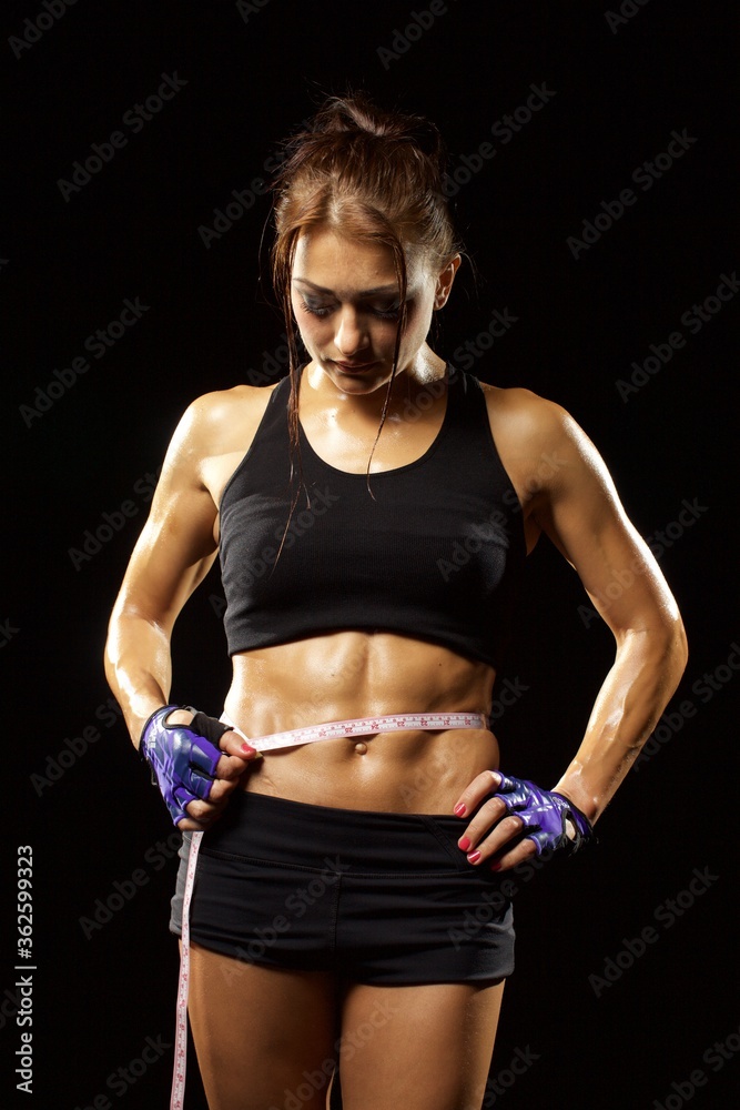 Naklejka premium Fitness woman in sportswear with ideal fitness body checking measuring tape