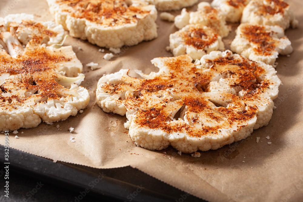 raw cauliflower steaks with spice on baking tray. plant based meat substitute