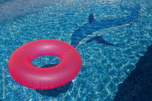 Flotador rosa flotando en el agua cristalina de una piscina azul con un delfín en un verano caluroso en España foto tomada a mediodía  photo