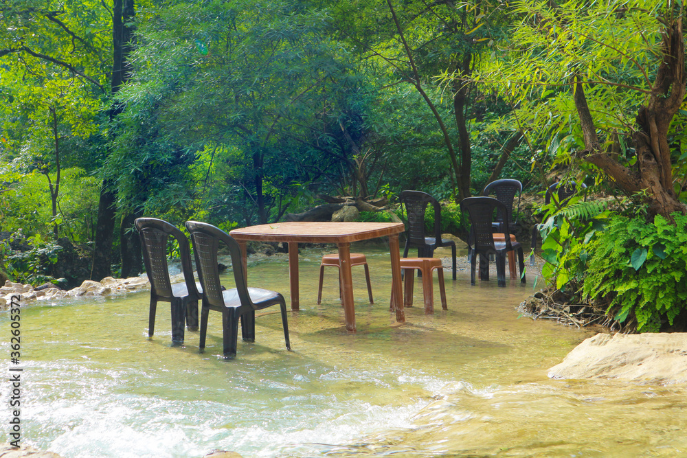 Tables and chairs of outdoor cafes in the waters of the waterfall. Romantic place in the Indian jungle. Waterfall in Rishikesh, India.
