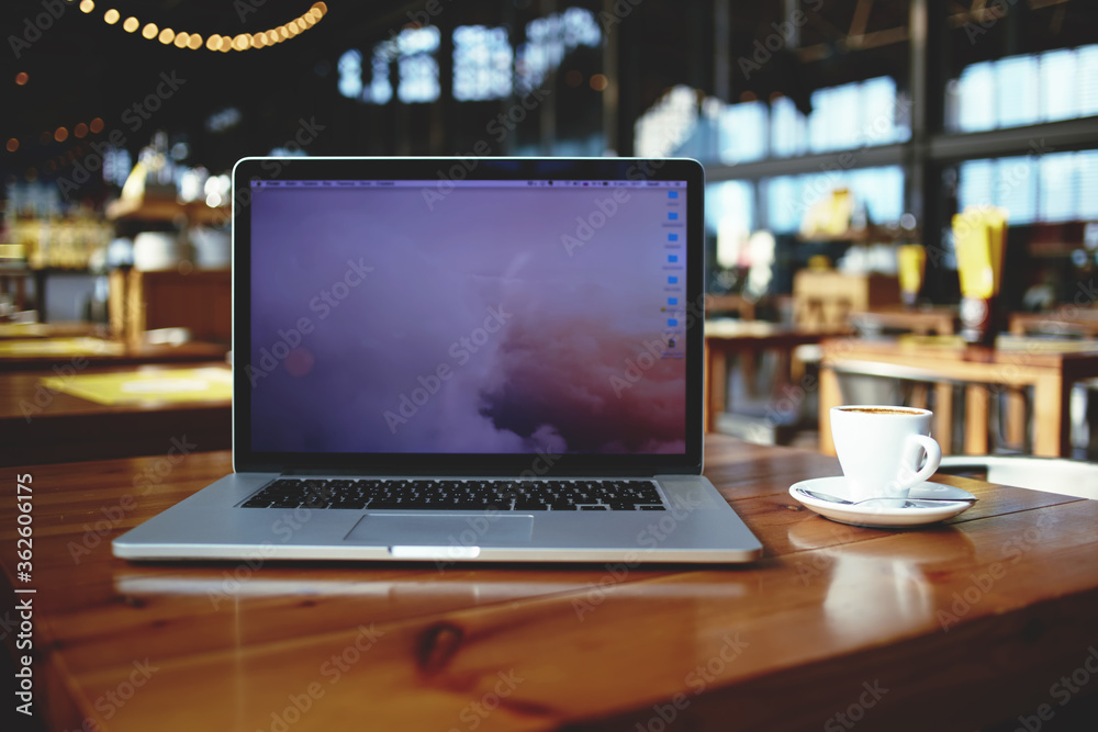 Open laptop computer and cup of coffee lying on a wooden table in cafe bar interior, portable net-book with copy space screen for your information content or text message, freelance work via internet Open laptop computer and cup of coffee lying on a wooden table in cafe bar interior, portable net-book with copy space screen for your information content or text message, freelance work via internet