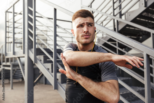 Image of unshaven athletic sportsman using earphones while working out