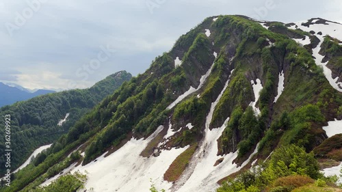 Panorama of spring mountains in the highlands of the Caucasus. Bright green young grass on the south slope. Snow melts in crevices. Beautiful clean nature.