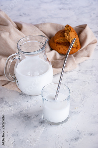 Glass jug and glass with milk on a light concrete background. Pieces of oatmeal cookies and a linen napkin. Home breakfast concept.