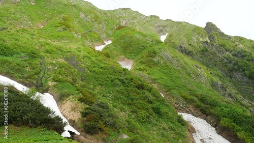Panorama of spring mountains in the highlands of the Caucasus. Bright green young grass on the south slope. Snow melts in crevices. Beautiful clean nature.