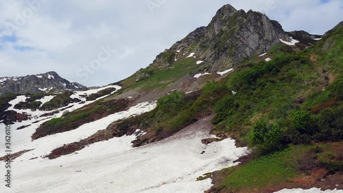 Alpine landscape. A huge glacier on the side of a mountain. The beginning of spring. The snow melts and opens up verdant slopes. Mountains of the Caucasus.