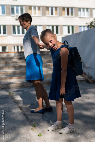A little unhappy girl with a backpack pulls her mother by the hand does not want to go to school. A woman leads a resisting daughter to school. The conflict of generations.
