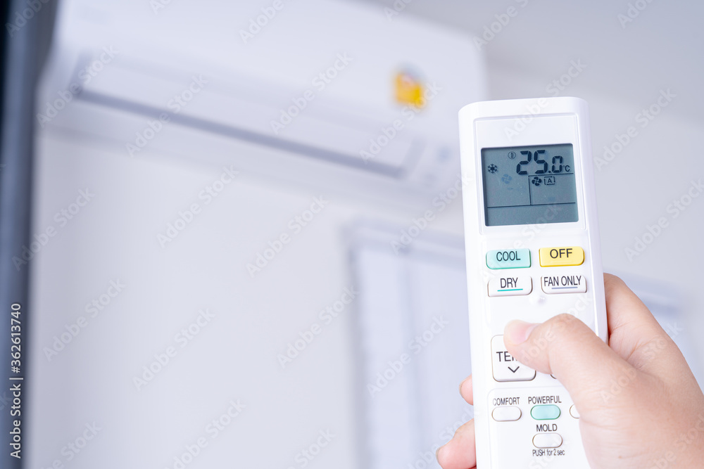 Human hand is using white remote of air conditioner for turn on or adjust temperature of air conditioner inside the room. Human hand is using white remote of air conditioner for turn on or adjust temperature of air conditioner inside the room.