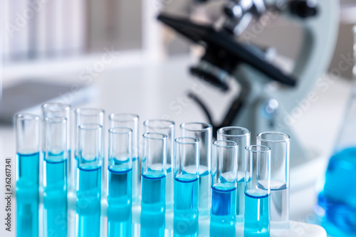 Test tubes with blue liquid in holder with microscope in background. Science glass equipment in laboratory for chemistry and medical research.