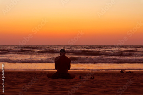 Silhouette of a man sitting in the lotus position on the shores of the Indian Ocean. Sunset in Gokarna, India.