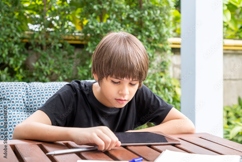 Cute boy using tablet while doing homework in garden at home Cute boy using tablet while doing homework in garden at home
