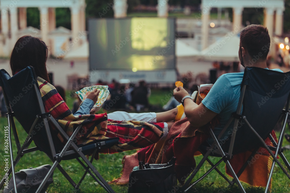 Φωτογραφία couple sitting in camp-chairs in city park looking movie outdoors at open air ci