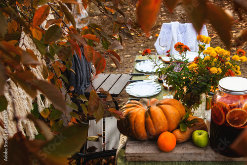 A festive autumn brunch among the yellow trees, with pumpkins, a yellow bouquet and pastries. Thanksgiving or family dinner in the backyard.