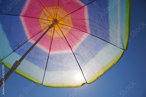 the sun shines through a multi-colored beach umbrella