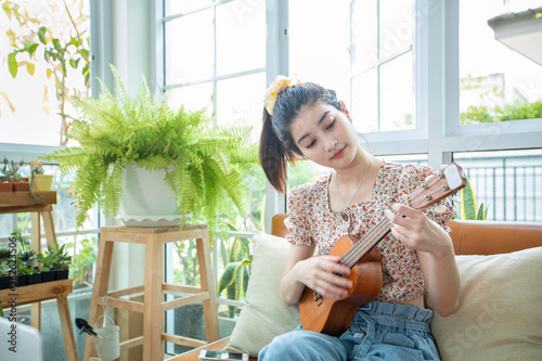 Asian women use their notebook computers to study and practice playing ukulele on the internet at home. photo