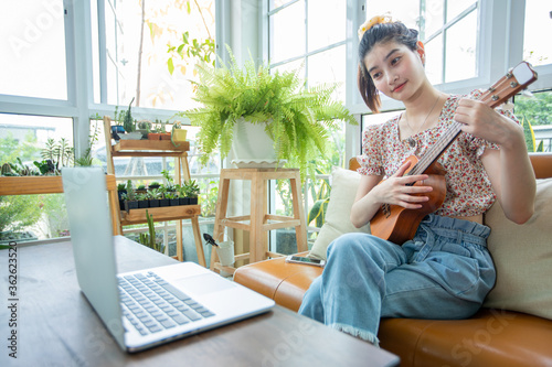 Asian women use their notebook computers to study and practice playing ukulele on the internet at home. photo