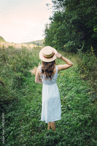 Girl in a hat and sundress outside the city. Young woman in a white summer board with a bouquet. Girl in a green summer field. © chdenisz