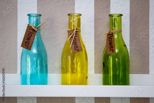 Drei verschieden farbige Glasflaschen stehen auf einem Regal.