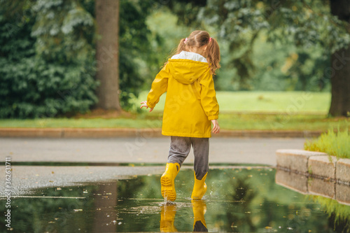 A girl in a yellow jacket and boots runs and jumps through puddles