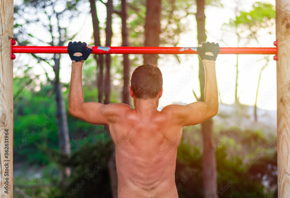 Back view of a man doing pull ups in park Back view of a man doing pull ups in park