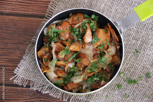 Fried chanterelles (roosters) with onions and fresh herbs in a small green pan on a linen napkin