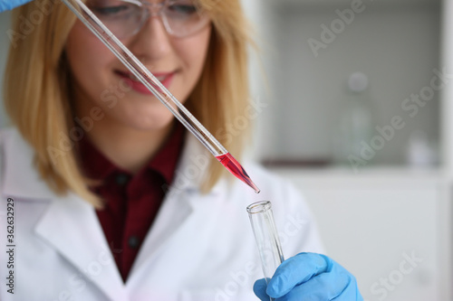Young pretty woman wearing glasses and holding reagent tube while conducting research in the laboratory